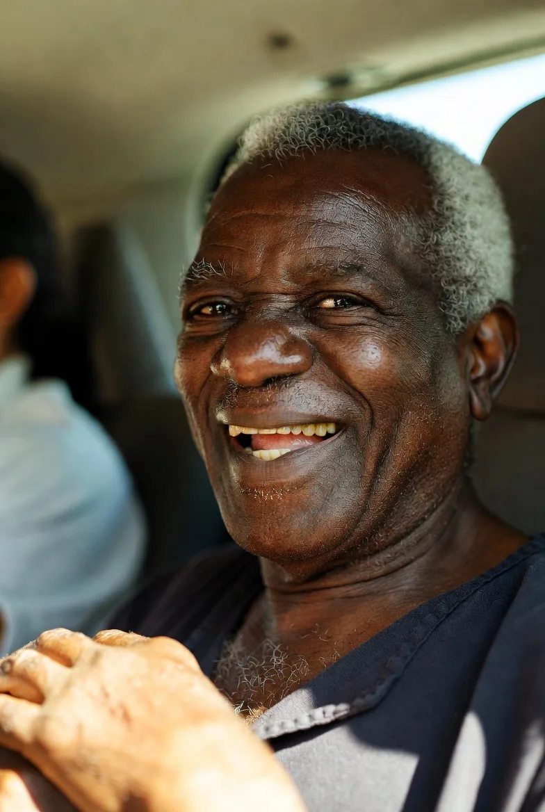Elderly Black man smiling joyfully inside the vehicle during his transport